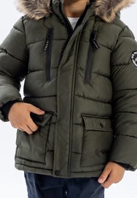 Puffige grüne Parka-Jacke mit gefütterter Kapuze, mit Reißverschluss versehenen Brusttaschen und zwei geknöpften Fronttaschen. Isoliermaterial mit Steppdetails.