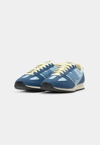 Blue and light blue retro sneakers with a suede and mesh upper, featuring laces, a rubber sole, and a distinctive N logo on the side.