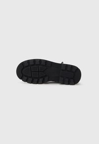 Suela de zapato de goma negra con surcos profundos y patrones multidireccionales. Presenta un talón reforzado y bordes lisos para mayor durabilidad.