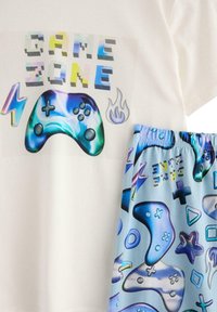 Korte mouwen witte t-shirt met de tekst "GAME ZONE" en een graphic van controllers; gecombineerd met blauwe shorts met kleurrijke gaming-iconen en vormen.