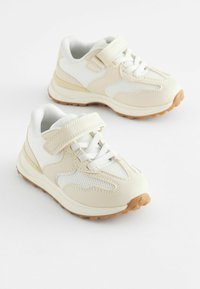 Jasne beżowe buty sportowe z materiałów siateczkowych i syntetycznej skóry, wyposażone w rzep, sznurowadła oraz teksturowaną gumową podeszwę.