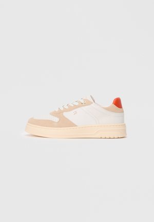 Sneakers con una toma in pelle bianca e accenti in camoscio beige, con una punta testurizzata, un'etichetta sul tallone arancione e una suola spessa di colore crema.