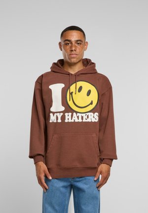 Brauner Kapuzenpullover mit einem großen gelben Smiley-Gesicht und weißem Text mit der Aufschrift "ICH LIEBE MEINE HASSER." Mit einer vorderen Tasche.