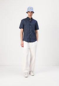 Chemise bleu marine à boutons avec un petit motif floral, associée à un pantalon large blanc et un chapeau seau bleu clair. Des baskets blanches complètent le look.
