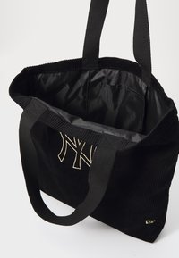 Μαύρη κοτλέ τσάντα ώμου με διπλές υφασμάτινες λαβές, διακοσμημένη με κεντημένο λογότυπο σε χρυσό. Λείος μαύρος επένδυση με εσωτερική τσέπη για οργάνωση.