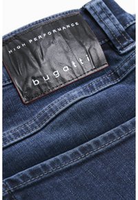 Mørkeblåt denimstof med en glat tekstur. Har en sort læderlap mærket "HIGH PERFORMANCE" med "bugatti" i hvid skrift.