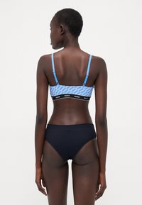 Blue patterned bralette with thin straps and black band featuring "Hugo" logo; paired with black high-waisted bikini briefs.
