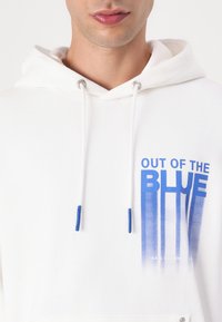 Felpa bianca con cappuccio e grafica in gradiente blu che recita "OUT OF THE BLUE." Presenta dettagli in metallo argentato e accenti blu sui lacci.