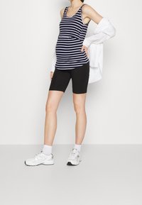 Pruhované námořnicky modré a bílé tílko s přiléhavým střihem, doplněné černými cyklistickými šortkami a bílými sportovními botami. Přehazovaná bílá oversized košile.