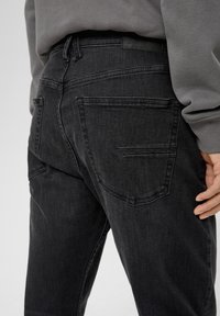 Black denim jeans with a fitted shape, featuring back pockets and subtle stitching details. Material has a soft texture and slight stretch.
