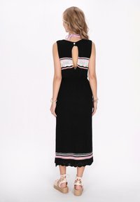 Rochie midi neagră cu o deschidere în spate în formă de cheie, accente brodate colorate, țesătură texturată și tiv ondulat, asortată cu espadrile deschise.