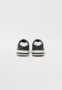 Marineblå sneakers med et teksturert mesh-overdel, mørke aksenter og beige gummisåler. Har et distinkt hældesign og logodetalj på baksiden.