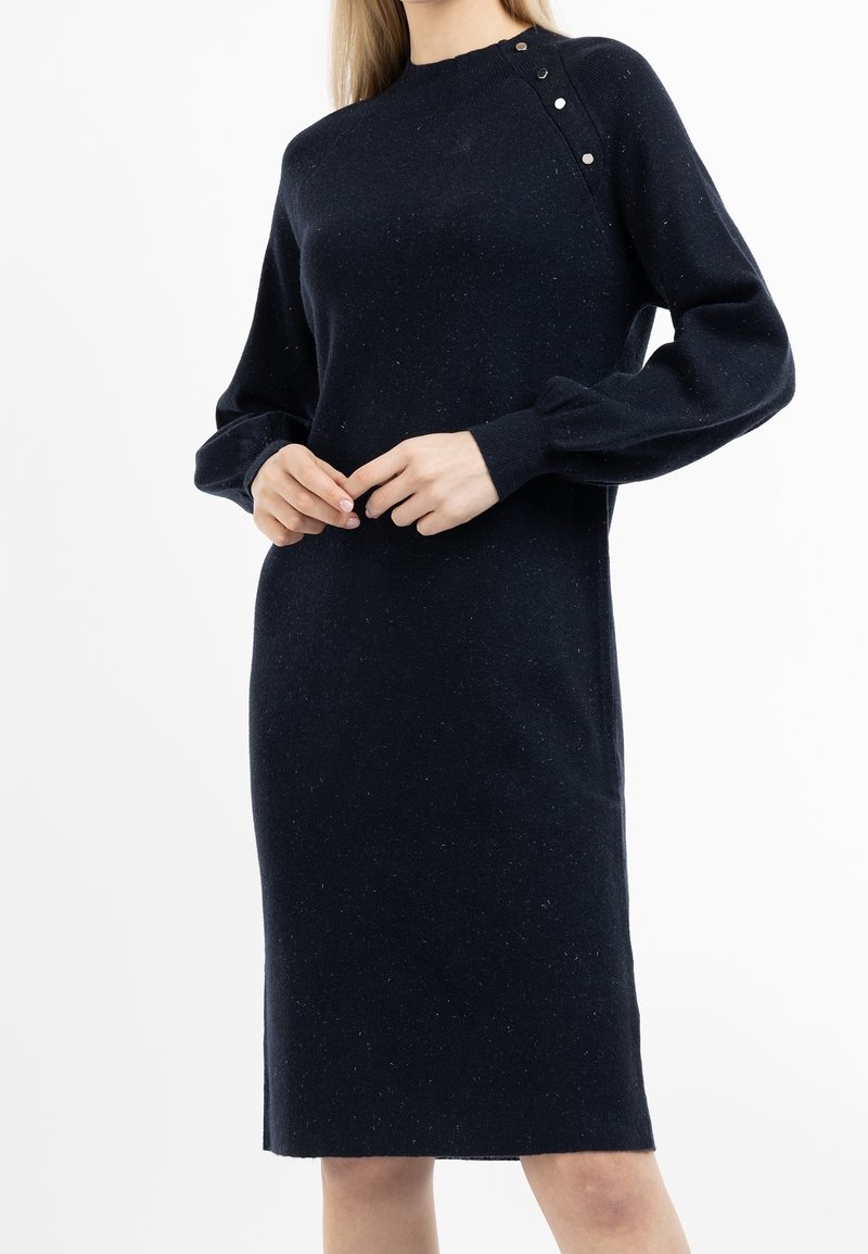 Strickkleid in Dunkelblau mit hohem Ausschnitt, langen Puffärmeln und drei dekorativen Knöpfen an der Schulter. Weicher, strukturierter Stoff.