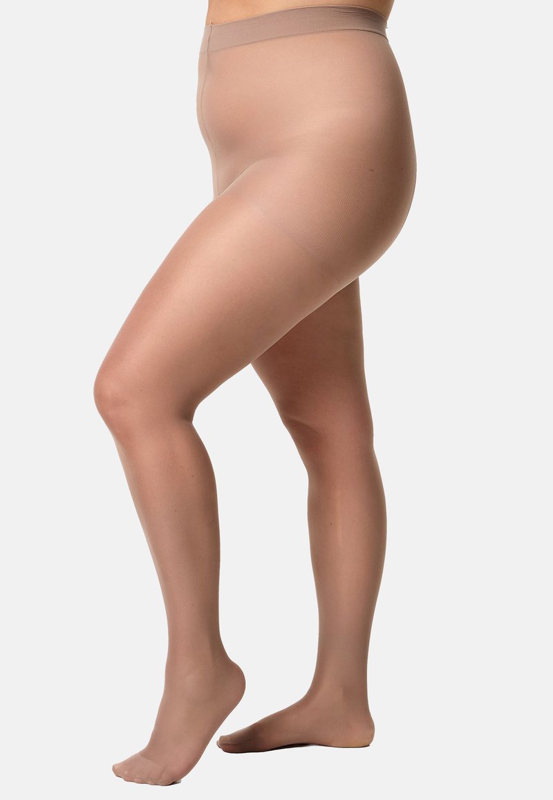Persona incinta che indossa collant premaman trasparenti color carne, in piedi con un piede sollevato su uno sfondo neutro.
