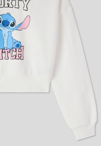 Felpa bianca tagliata con un personaggio dei cartoni animati blu sul davanti, con la scritta "DIRTY BITCH" in nero e rosa. Polsini e orlo a costine.