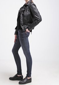 Chaqueta de motociclista de cuero negro, jeans oscuros ajustados y zapatos negros de cordones; presenta una textura suave y un diseño casual.