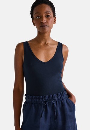 Haut sans manches bleu marine avec un col en V, fabriqué en tissu doux. Associé à un pantalon bleu marine ample et texturé avec une taille froncée.