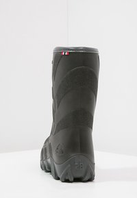 Schwarzer Gummistiefel mit strukturierter Oberfläche, gepolstertem Absatz und niedrigem Profil. Mit einem kleinen roten, weißen und blauen Flaggenmotiv auf der Rückseite.
