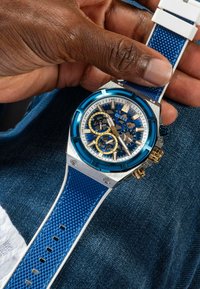 Blaues Chronographuhr mit einem Gehäuse aus rostfreiem Stahl, strukturiertem blauen Silikonarmband, goldenen Akzenten und einem detaillierten blauen und weißen Zifferblatt.