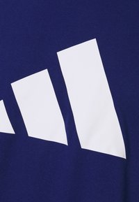 Námořnická modrá bavlněná látka s velkým bílým grafickým logem, skládajícím se ze tří diagonálních pruhů, hladká textura a moderní design.