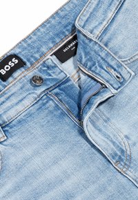Jeans in denim azzurro chiaro con vestibilità slim, dotati di chiusura a bottone, zip e dettagli in cucitura marrone. Etichetta del marchio visibile all'interno.