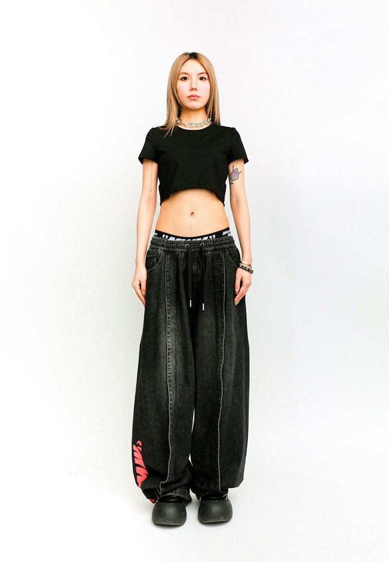 Camiseta negra corta y pantalones vaqueros sueltos negros con gráficos rojos. Los pantalones cuentan con una cinturilla elástica y cordón ajustable. Textura suave.