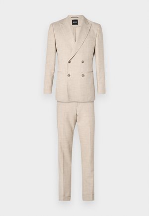 Costume beige à double boutonnage avec un tissu texturé, pantalon slim-fit, et deux poches avant sur la veste. Étiquette de marque visible à l'intérieur du col.