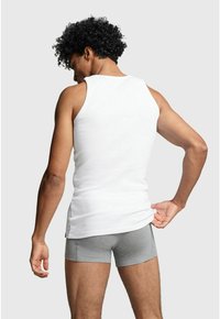 White tank top made of cotton, featuring a sleeveless design. Paired with gray shorts, displaying a fitted silhouette.