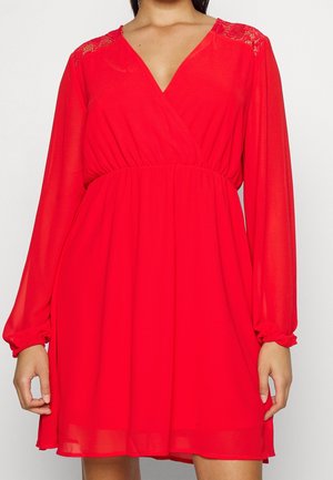 Red long-sleeve dress with V-neck, gathered waist, and lace details on shoulders, worn by a standing person.