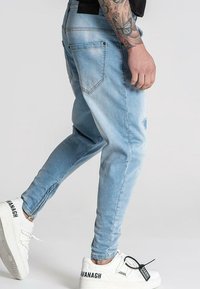 Ljust blå denimjeans med en åtsittande design, synliga sömmar och slitna detaljer. Mjuka med vita sneakers med svarta accenter.