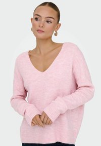 Lichtroze gebreide trui met een diepe V-hals, geribde manchetten en een losse pasvorm. Zachte textuur met een licht pluizig uiterlijk.