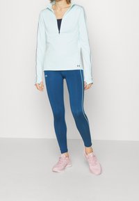 Jasnoniebieska, długosuwakowa bluzka, granatowe legginsy z bocznymi paskami oraz różowe buty sportowe. Gładki materiał, dopasowany krój, sportowy styl.