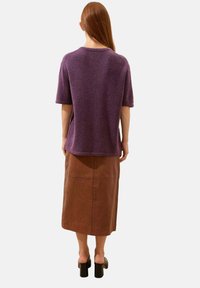 Krótki rękaw, fioletowa dzianinowa bluzka o luźnym kroju, w połączeniu z brązową spódnicą midi. Gładka tekstura i minimalne detale na całej powierzchni.