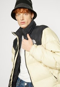 Pufferjack met een zwart en crèmekleurig kleurenschema, ritssluiting, hoge kraag en geribbelde manchetten. Gestyled met een witte shirt en denim.