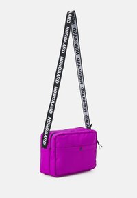 Fialová polstrovaná crossbody taška se zipovým uzávěrem, nastavitelným černým popruhem s logem "Nørgaard" a přední kapsou na patentku.