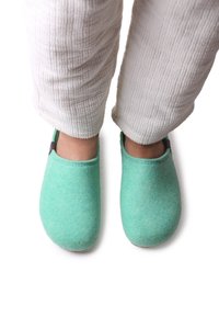 Gröna filtsandaler med en slät yta, rund form och sömdetaljer, i kombination med vita, texturerade byxor.