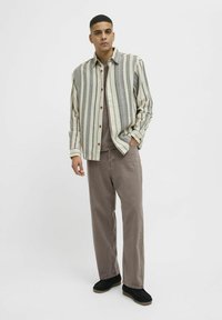Ribbet, letvægts skjorte med knapper i beige og grå, parret med brune lige benbukser og sorte sko. Minimalistisk design.