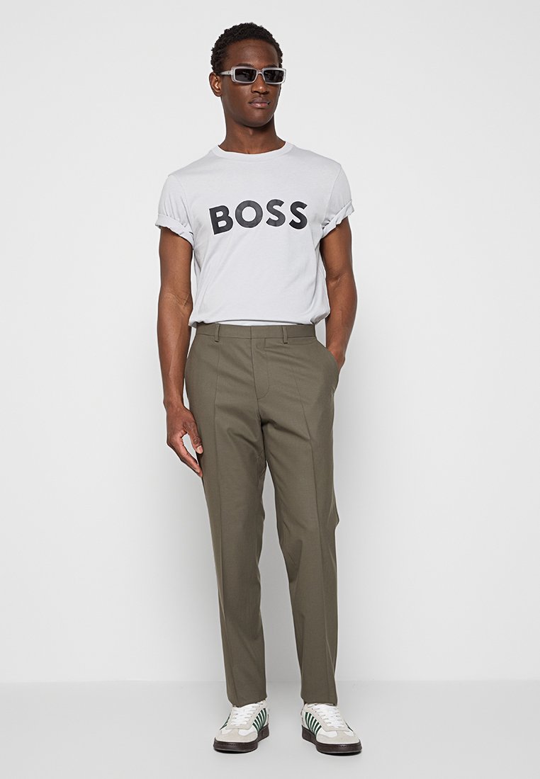 Camiseta blanca con "BOSS" en letras negras en negrita, combinada con pantalones oliva y zapatillas blancas con rayas verdes y negras.