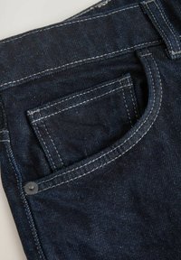 Donkerblauwe denim jeans met een voorzak met zichtbare stiksels en een metalen klinknagel. De stof heeft een getextureerd, licht vervaagd oppervlak.