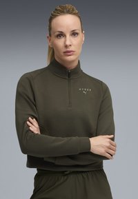 Pullover a mezzo zip di colore verde oliva scuro, aderente e con colletto alto. Realizzato in tessuto morbido, presenta tasche laterali e una stampa logo discreta sul petto.