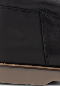 Stivale in pelle nera con texture liscia, che si fonde in una suola in gomma beige. Presenta un logo impresso di lato e dettagli di cucitura minimi.