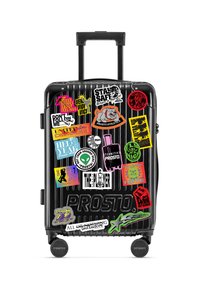 Czarna walizka na kółkach z żebrowanym wzorem. Ozdobiona kolorowymi naklejkami z różnymi grafikami i tekstami.