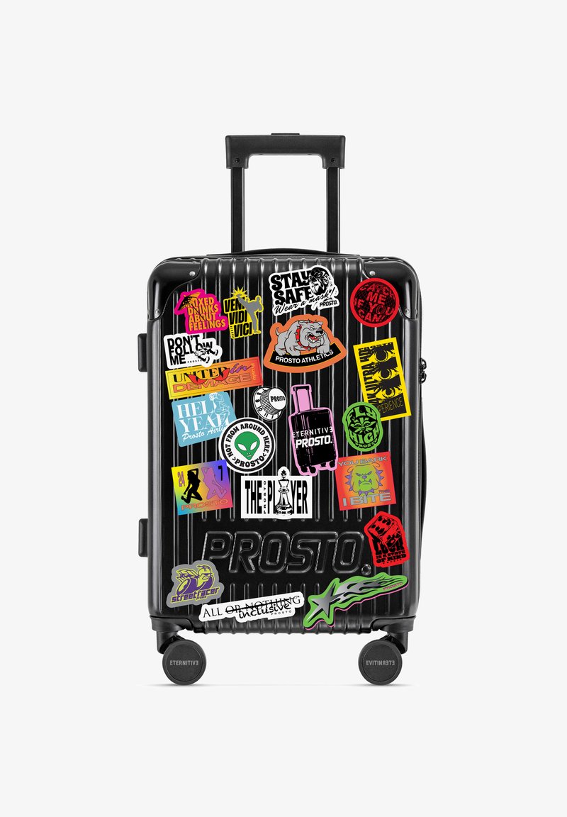 Czarna walizka na kółkach z żebrowanym wzorem. Ozdobiona kolorowymi naklejkami z różnymi grafikami i tekstami.