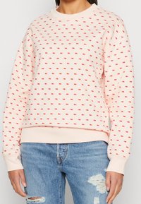 Felpa rosa chiaro con motivi geometrici rossi sparsi, polsini e scollatura a costine. Abbinata a jeans in denim blu effetti vissuti.