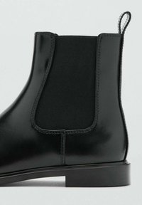 Bottines Chelsea en cuir noir avec des panneaux latéraux élastiques, finition lisse, talon bas et une languette à l'arrière pour un enfilage facile.