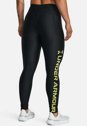 Zwarte leggings van rekbaar materiaal met een hoge tailleband. Voorzien van een gele "Under Armour"-logo en zijkanten met accenten. Gladde textuur.