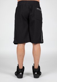 Zwarte textuurshorts met een elastische tailleband en zijstrepen. Het achterzak heeft de branding "GORILLA MEN" in het wit. Gemaakt in combinatie met zwarte schoenen.