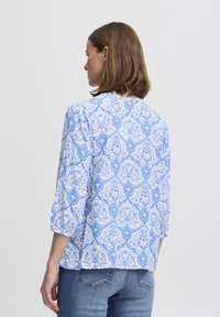 Camicia a fiori blu e bianca con maniche a tre quarti, tessuto leggero, scollatura rotonda e vestibilità ampia, abbinata a jeans in denim.