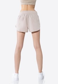 Shorts da donna beige realizzati in materiale leggero con un elastico in vita, dotati di spacchi laterali e una vestibilità comoda.