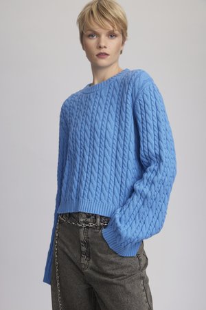 Light blue cable-knit sweater with a round neck, ribbed cuffs, and a loose fit, paired with dark jeans featuring a silver chain accent.